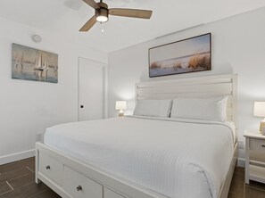 A bedroom with a bed, two bedside tables, a ceiling fan, and two wall-mounted lamps.