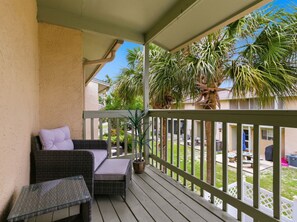 A balcony with wicker furniture, a potted plant, and a view of a residential area with palm trees.