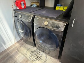 Ein Waschraum mit zwei Waschmaschinen mit Frontlader, einem roten Reinigungsmittel und einer handgeschriebenen Nachricht auf dem Boden.