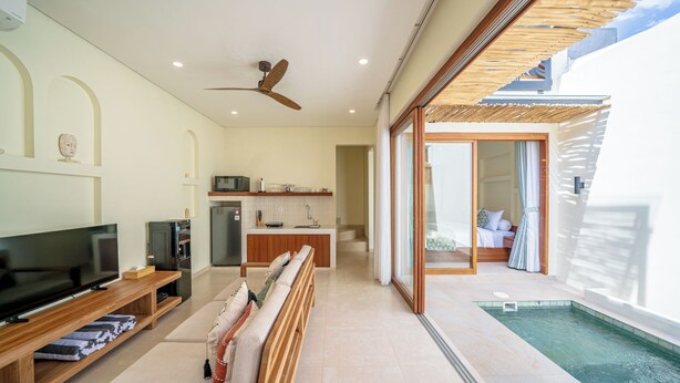 A modern living room with a TV, seating area, kitchen, and a pool. - Villa Aurora Canggu (Canggu)