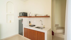 A compact kitchen with a microwave, sink, and wooden cabinets. - Villa Aurora Canggu (Canggu)