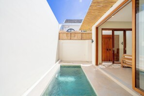 A modern pool area with a clear blue pool, a wooden deck, and a glass door leading to a room. - Villa Aurora Canggu (Canggu)
