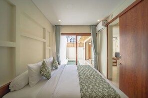 A hotel room with a bed, a wooden wardrobe, a small table, and a view of a pool area. - Villa Aurora Canggu (Canggu)