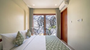 A hotel room with a bed, curtains, an air conditioning unit, and a view through a window with a leaf pattern. - Villa Aurora Canggu (Canggu)