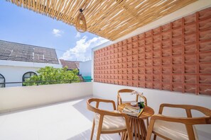 A balcony with a wooden ceiling, a cushioned wall, and a table with chairs. - Villa Aurora Canggu (Canggu)