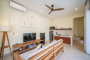 A modern living room with a TV, sofa, and wooden furniture. A kitchen with a microwave and refrigerator is visible in the background. - Villa Aurora Canggu (Canggu)