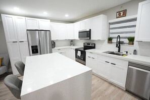 A modern kitchen with white cabinetry, stainless steel appliances, and a central island. - Mango Tree House (Hialeah)
