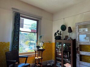 Ein Zimmer mit Fenster, einem Sessel, einem Bücherregal und einer Lampe.