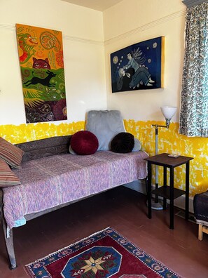 Ein Zimmer mit einer Couch, einem kleinen Tisch, einer Lampe und zwei Bildern an der Wand.