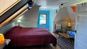 A bedroom with a sloped ceiling, a bed, a chair, a table, and a window with a view. - Art filled 1908 house in Columbia City, close to Light Rail. Cozy, relaxing, fun (Seattle)