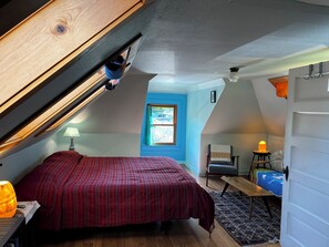 Ein Schlafzimmer mit schrägen Wänden, einem Bett, einem Sessel, einem Tisch und einem Fenster mit Blick.