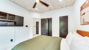 Un dormitorio con una cama, ventilador de techo, televisión y dos puertas.