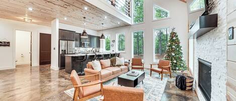 A spacious living area with a fireplace, a kitchen in the background, and a Christmas tree.