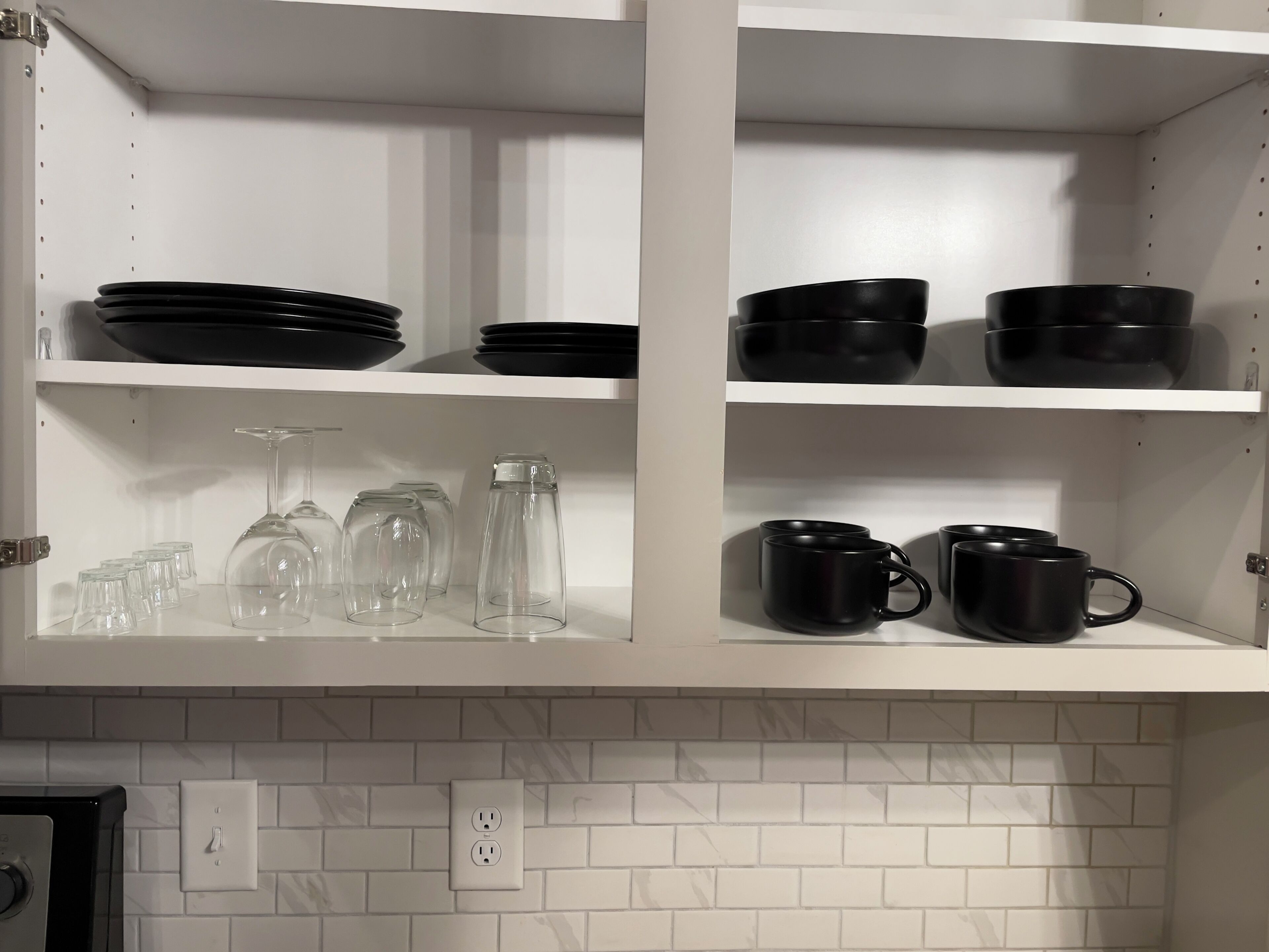 Une cuisine avec des armoires blanches, des bols noirs, des verres à vin et des tasses noires.