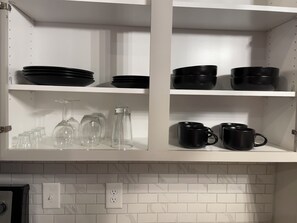 Une cuisine avec des armoires blanches, des bols noirs, des verres à vin et des tasses noires.