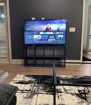 A flat-screen TV mounted on a black entertainment unit with a chevron-patterned shelf below. - Cozy 1-bedroom apartment in beautiful Atlanta Perfect for Long-term stays (Atlanta)