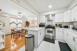 A modern kitchen with white cabinetry, a stainless steel stove, and a dining area with wooden chairs. - Charming 3BR Home Near NYC  Free Parking (JERSEY CITY)