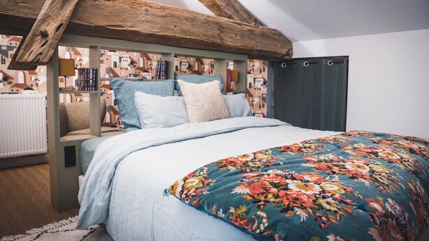 Une chambre à coucher avec un lit, une tête de lit en bois, une couvre-lit à motifs floraux et un papier peint à motifs.