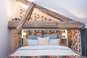 Een slaapkamer met een schuine kap, een bed met een bloemenbedekker en behang met een patroon.