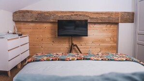 Une chambre à coucher avec une tête de lit en bois, un lit recouvert d’une couvre-lit à motifs floraux, une commode blanche et un téléviseur à écran plat fixé sur la tête de lit.