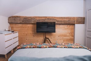 Een slaapkamer met een houten hoofdbord, een bed met een bloemenbedekking, een witte dressoir en een flatscreen televisie bevestigd aan het hoofdbord.