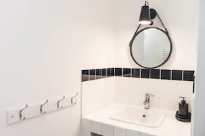 Een badkamer met een witte wastafel, een zwart-wit betegelde spatwand, een ronde spiegel, een wandlamp en een zeepdispenser.