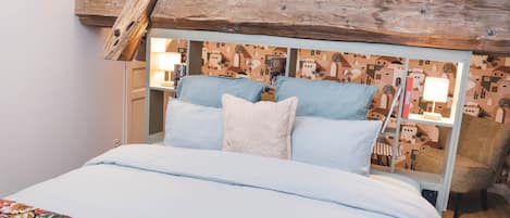 A bedroom with a bed, pillows, a nightstand, a lamp, and a chair.