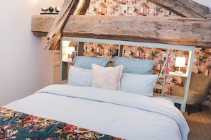 Een slaapkamer met een bed, kussens, een nachtkastje, een lamp en een stoel.