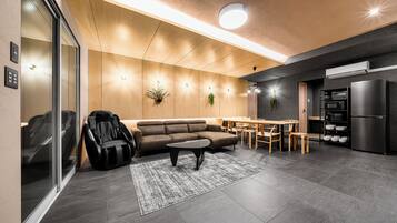 Una sala de estar moderna con un sofá, sillón de masaje y una zona de comedor con mesa y sillas.