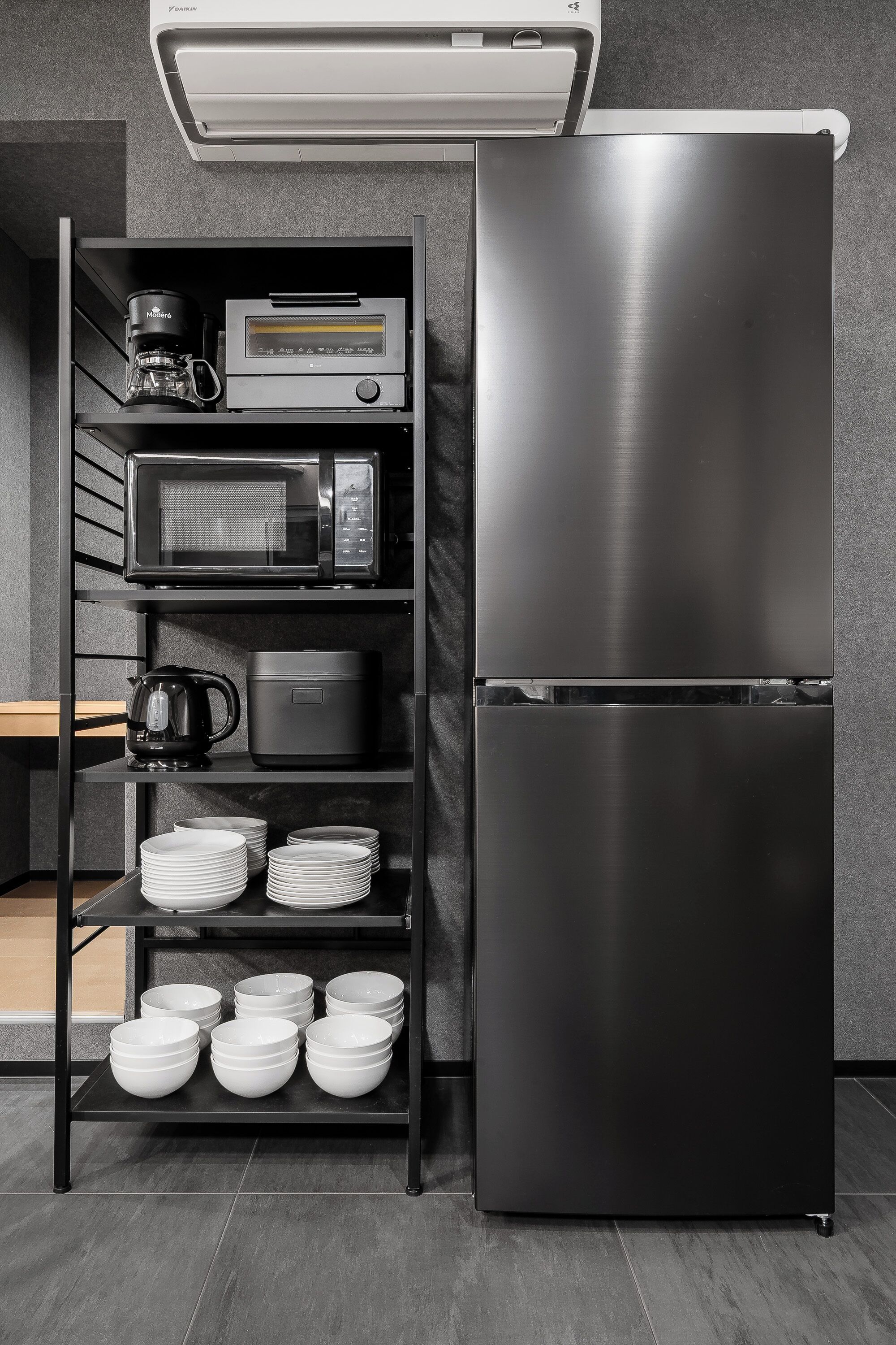 A kitchen with a stainless steel refrigerator, a coffee maker, a microwave, and shelves with plates and bowls.