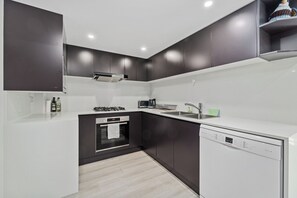 A modern kitchen with dark cabinetry, a built-in oven, a dishwasher, and a countertop with a kettle and a toaster. - Newly Renovated Spacious Apartment (North Sydney)