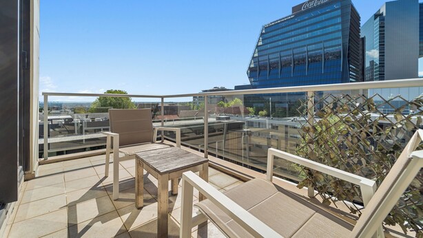 Una terraza en la azotea con barandilla de cristal, una mesa de madera y una silla.