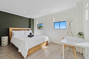 Ein modernes Schlafzimmer mit einem Holzbett, weißer Bettwäsche, einem kleinen Schreibtisch, einem Stuhl und einem Topfpflanzen.