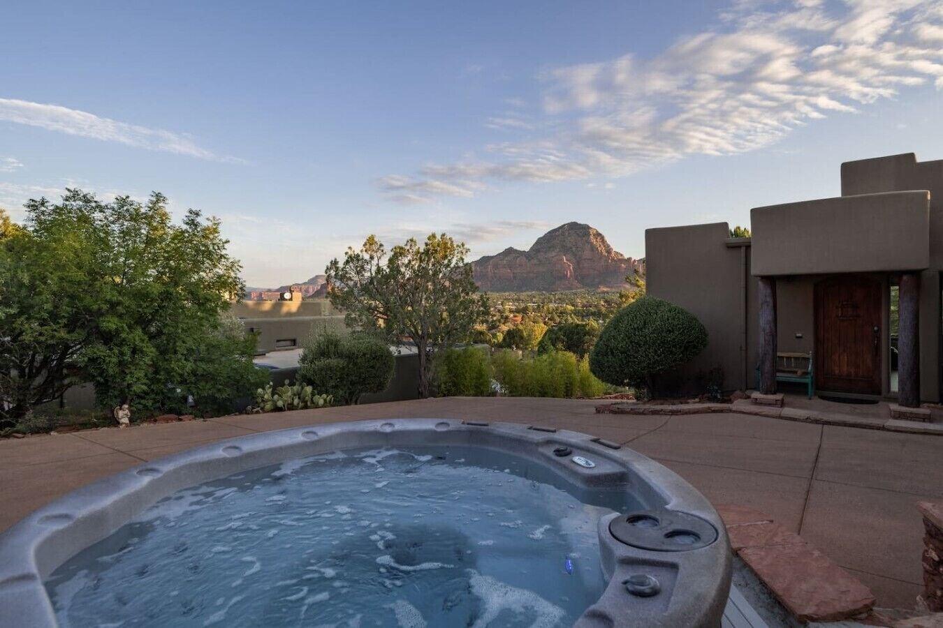 Un bain à remous avec vue sur les montagnes, entouré de verdure et adossé à un bâtiment doté d’une porte en bois.