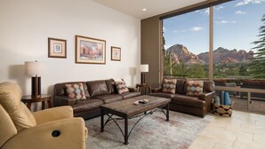 A spacious living room with a large window offering a mountain view, a brown leather sofa, a coffee table, and a beige armchair. - Sedona Jewel | Panoramic Views, Patio, Hot Tub (Sedona)