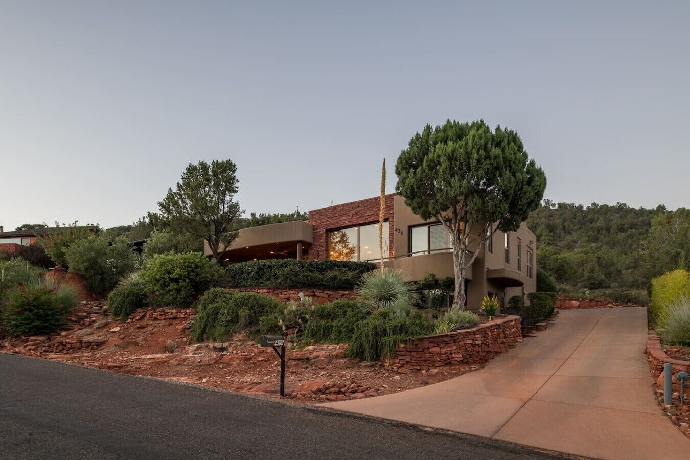 A modern two-story house with a stone facade, surrounded by landscaped gardens and a paved driveway.
