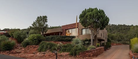 Una casa moderna de dos pisos con fachada de piedra, rodeada de jardines ajardinados y un camino pavimentado.