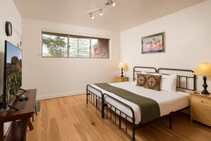 A bedroom with a bed, bedside tables, a desk, a television, and a window with a view of trees. - Sedona Jewel | Panoramic Views, Patio, Hot Tub (Sedona)