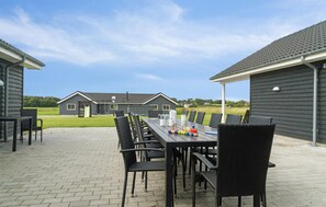 An outdoor patio with a long table and chairs, a playground in the background, and a grassy field. - Cozy home in Stege with sauna (Stege)