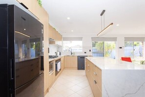Eine moderne Küche mit großem Kühlschrank, Herd und Geschirrspüler, Holzschränken und einer Marmorarbeitsplatte.