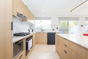 A modern kitchen with wooden cabinets, a gas stove, a dishwasher, and a window providing natural light. - Urban Comfort - Close to Fremantle (Hilton)