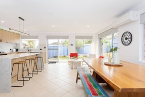 A modern kitchen with a bar area, a dining table with benches, and a large window. - Urban Comfort - Close to Fremantle (Hilton)