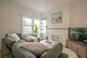 A living room with a grey sofa set, a white fireplace, and a television. - Comfortable Family Home in Newstead (Newstead)