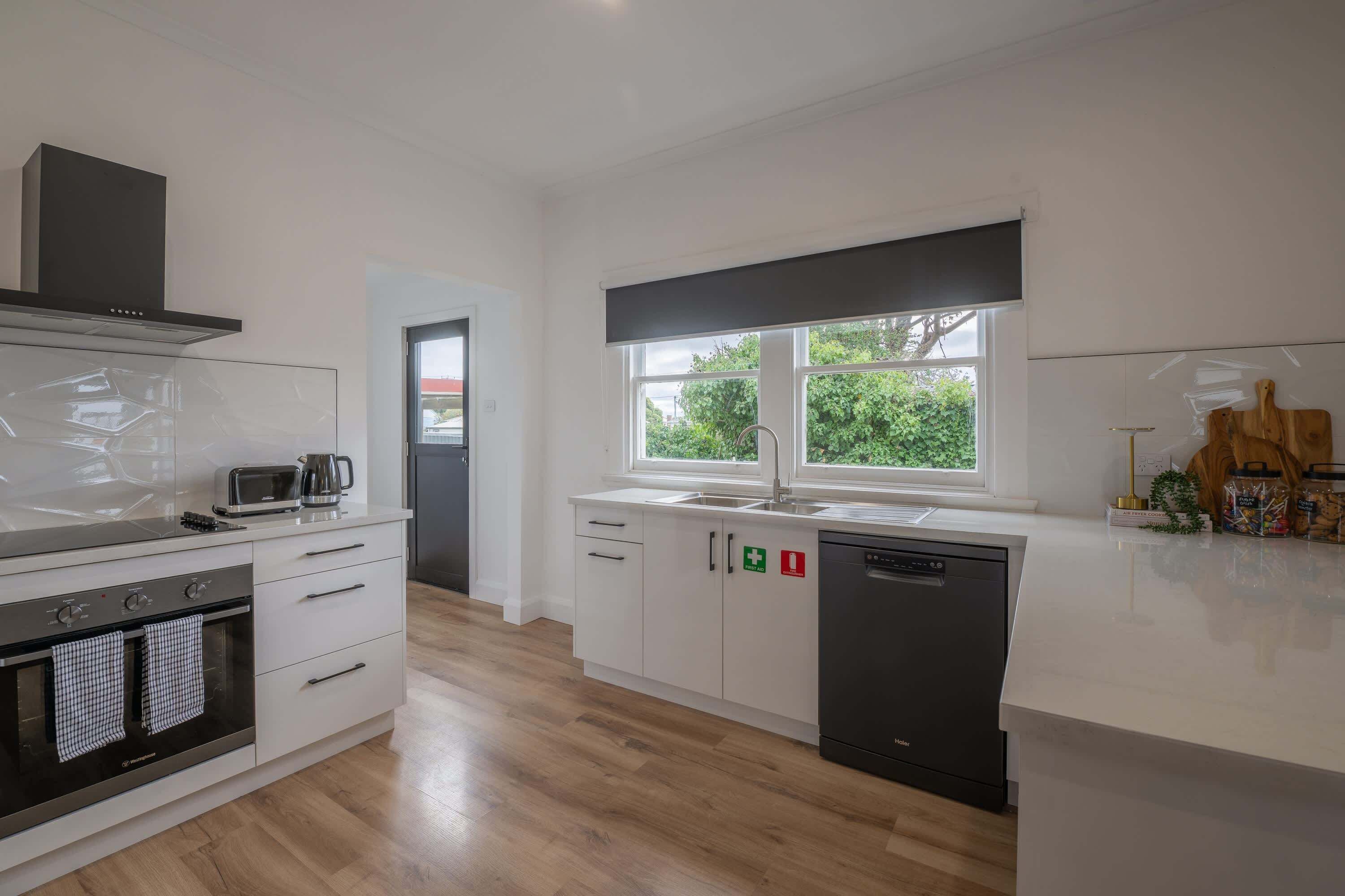 A modern kitchen with white cabinetry, a built-in oven, a dishwasher, and a window providing natural light.