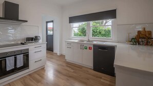 A modern kitchen with white cabinetry, a built-in oven, a dishwasher, and a window providing natural light. - Comfortable Family Home in Newstead (Newstead)