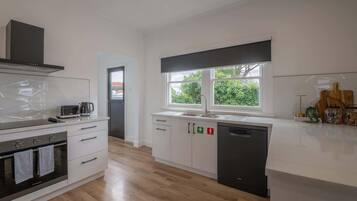 A modern kitchen with white cabinetry, a built-in oven, a dishwasher, and a window providing natural light.