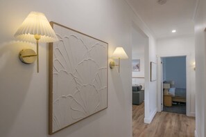 Um corredor com um painel decorativo na parede e duas luminárias fixadas.