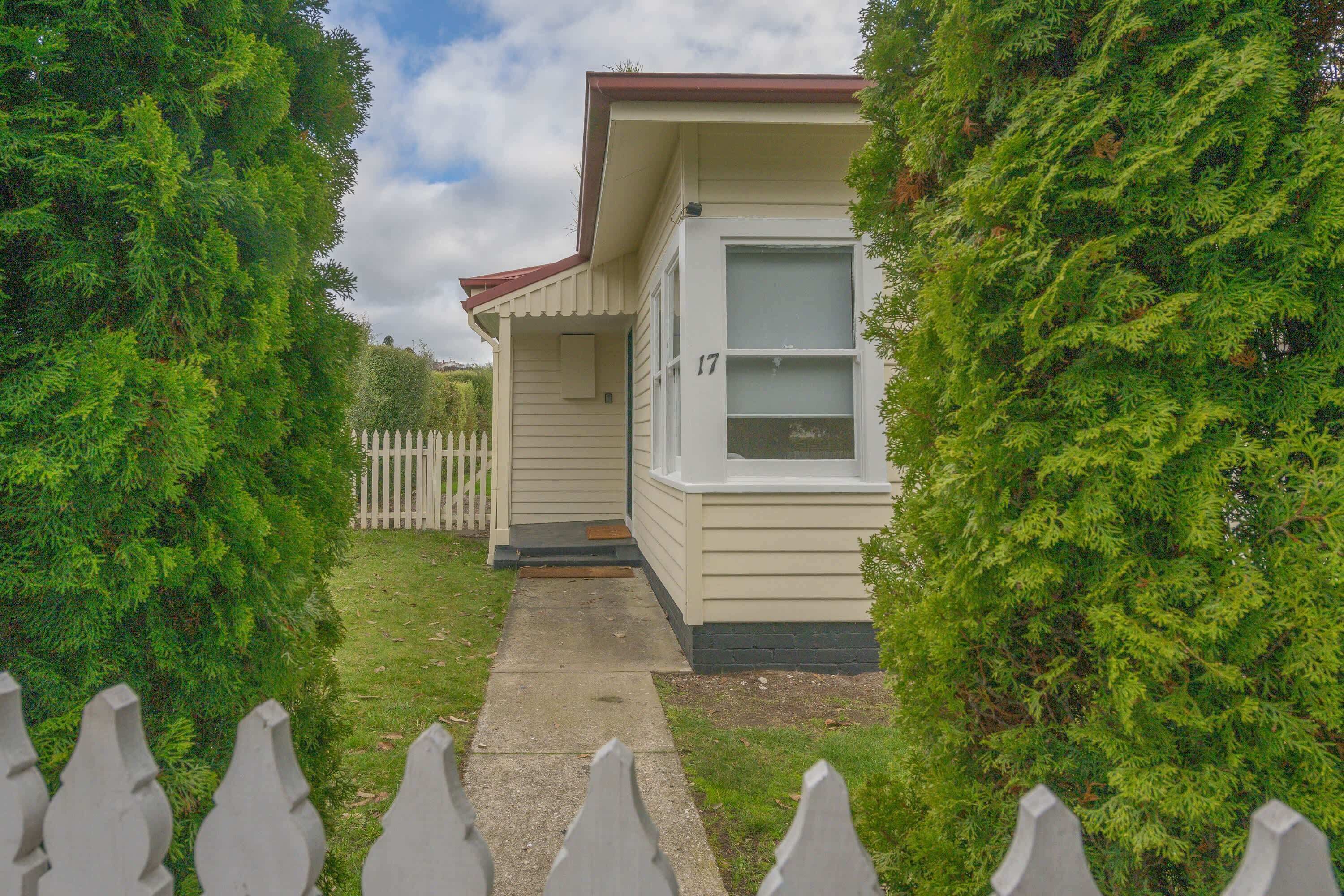 A single-story house with a front porch, a picket fence, and a number 17 on the door.