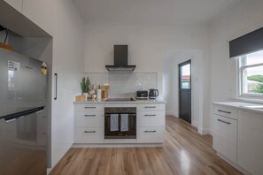 A modern kitchen with white cabinetry, a built-in oven, a microwave, and a coffee maker. - Comfortable Family Home in Newstead (Newstead)