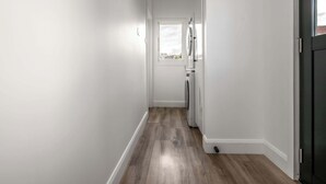 A narrow hallway with a wooden floor, a white door at the end, and a window with a view of the outside. - Comfortable Family Home in Newstead (Newstead)